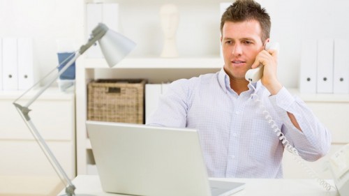 Мужчина с телефоном в руке за ноутбуком