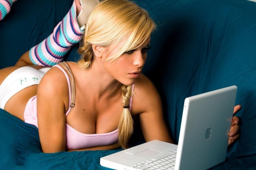 Красивая блондинка лежит на диване за ноутбуком