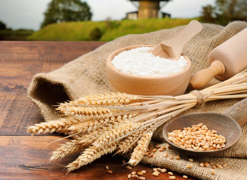 Мука, зерно, скалка и пшеничные колосья лежат на столе