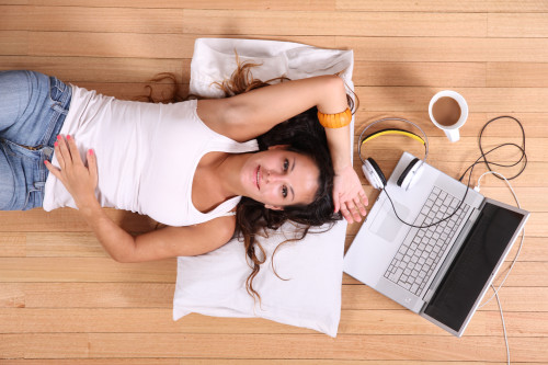 Девушка лежит на полу, а рядом с ней ноутбук и чашка с кофе