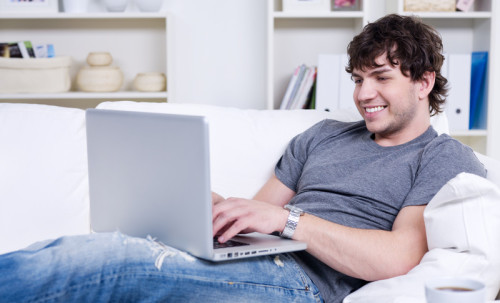 Парень сидит на диване за ноутбуком