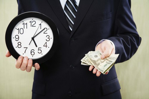 Парень в костюме держит в руках часы и деньги (доллары)